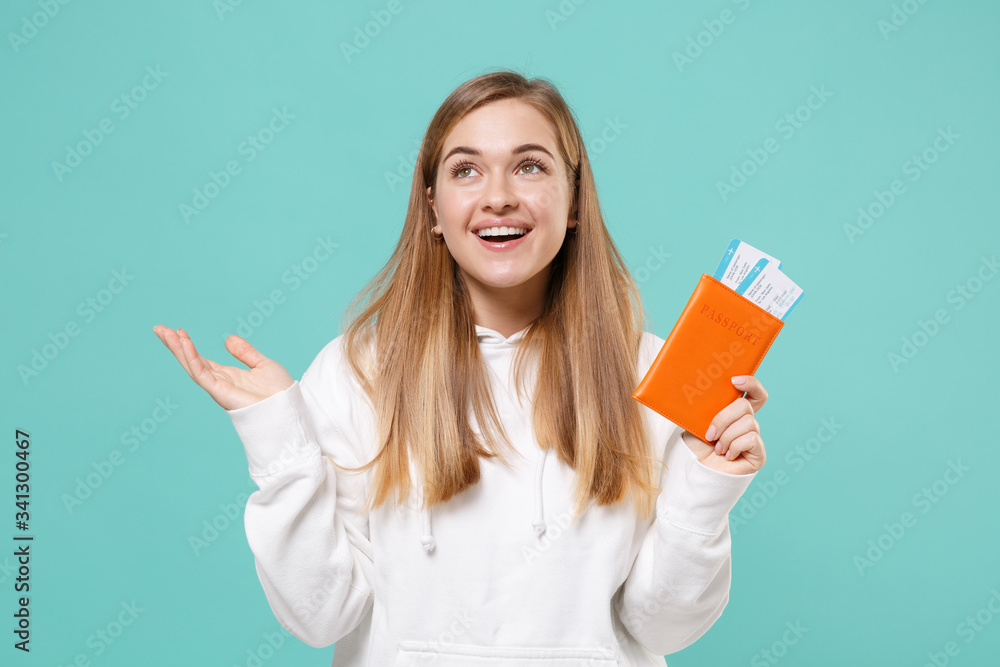 Smiling young woman girl in casual white hoodie posing isolated on blue turquoise background studio. People lifestyle concept. Mock up copy space. Hold passport tickets boarding pass, spreading hands. Smiling young woman girl in casual white hoodie posing isolated on blue turquoise background studio. People lifestyle concept. Mock up copy space. Hold passport tickets boarding pass, spreading hands.