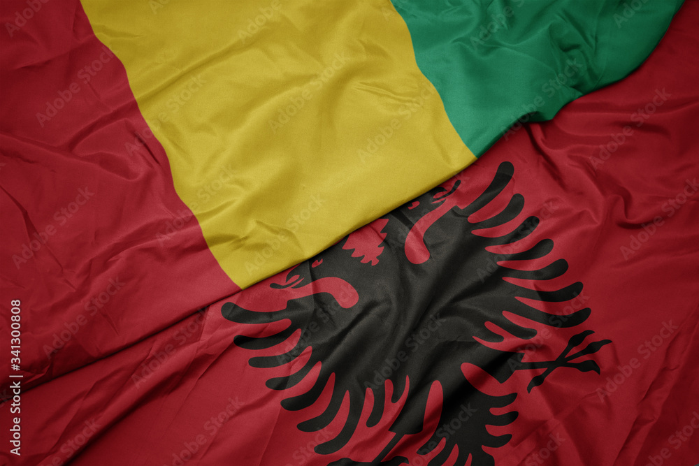 waving colorful flag of albania and national flag of guinea.