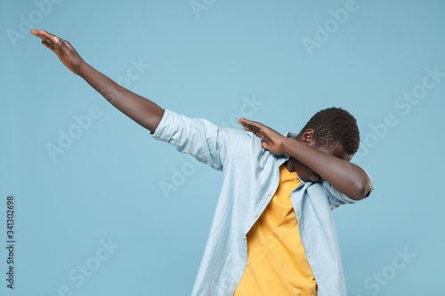 Young african american man guy in casual shirt, yellow t-shirt posing isolated on blue background studio portrait. People emotions lifestyle concept. Mock up copy space. Showing DAB dance gesture.