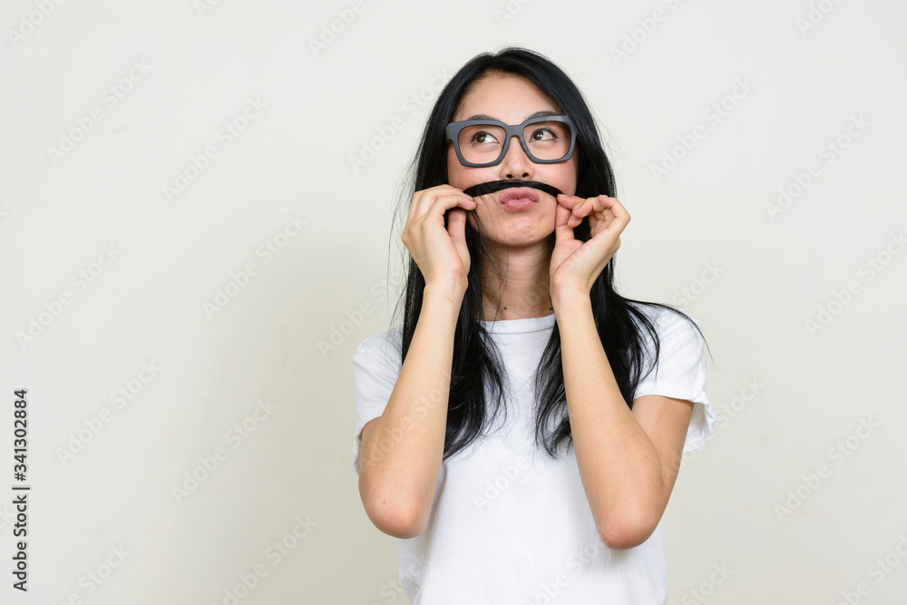 Young beautiful Asian nerd woman thinking and playing with hair as mustache Young beautiful Asian nerd woman thinking and playing with hair as mustache