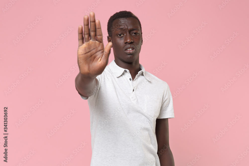Displeased young african american man guy in white polo shirt posing isolated on pastel pink background studio portrait. People lifestyle concept. Mock up copy space. Showing stop gesture with palm. Displeased young african american man guy in white polo shirt posing isolated on pastel pink background studio portrait. People lifestyle concept. Mock up copy space. Showing stop gesture with palm.