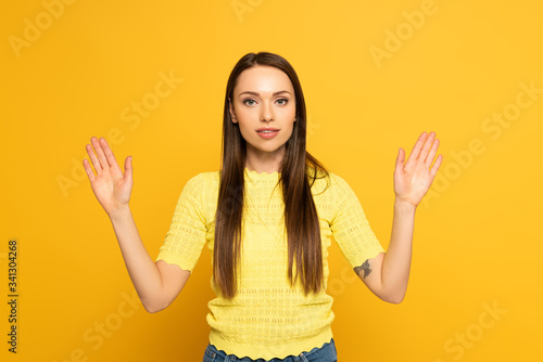 Young woman looking at camera while using sign language on yellow background