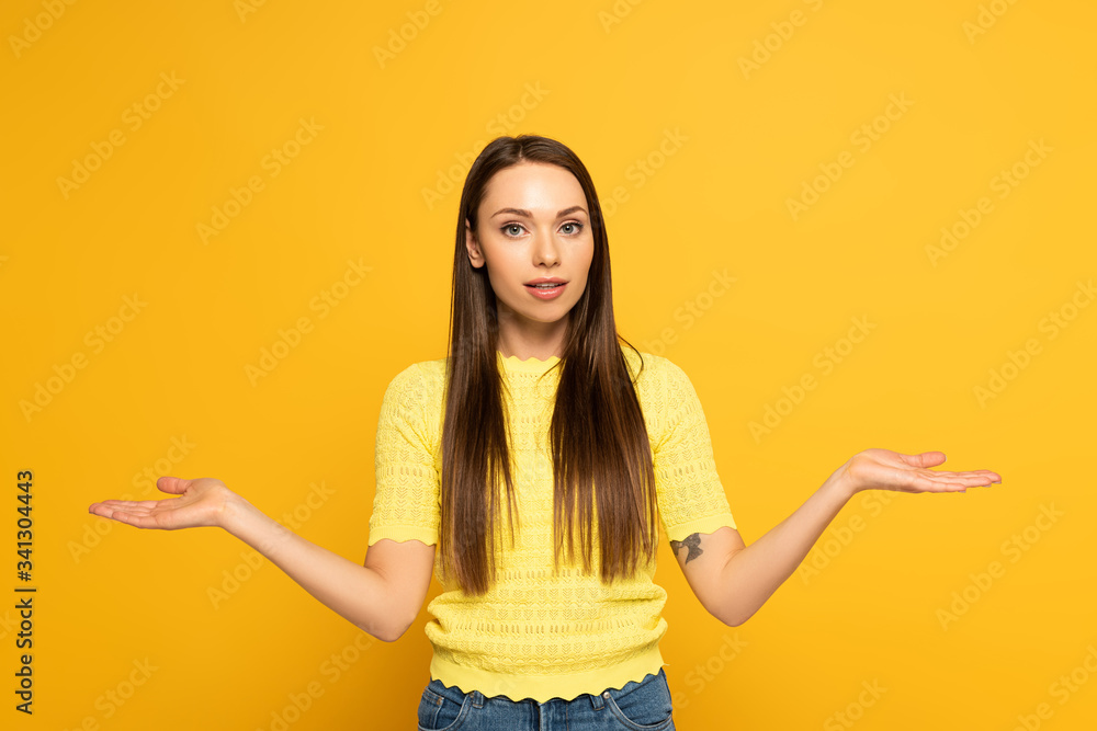 Attractive girl showing shrug gesture on yellow background Attractive girl showing shrug gesture on yellow background