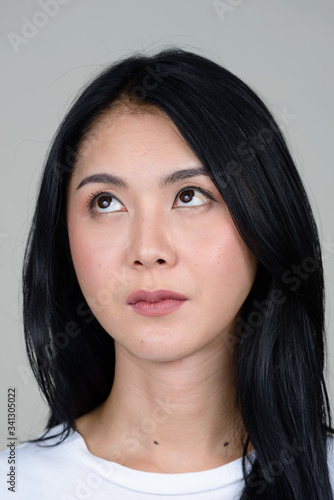 Face of young beautiful Asian woman thinking and looking up