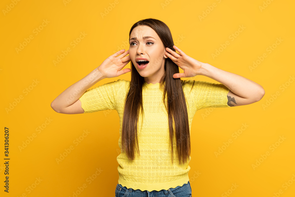 Worried woman with hands near ears looking away on yellow background Worried woman with hands near ears looking away on yellow background