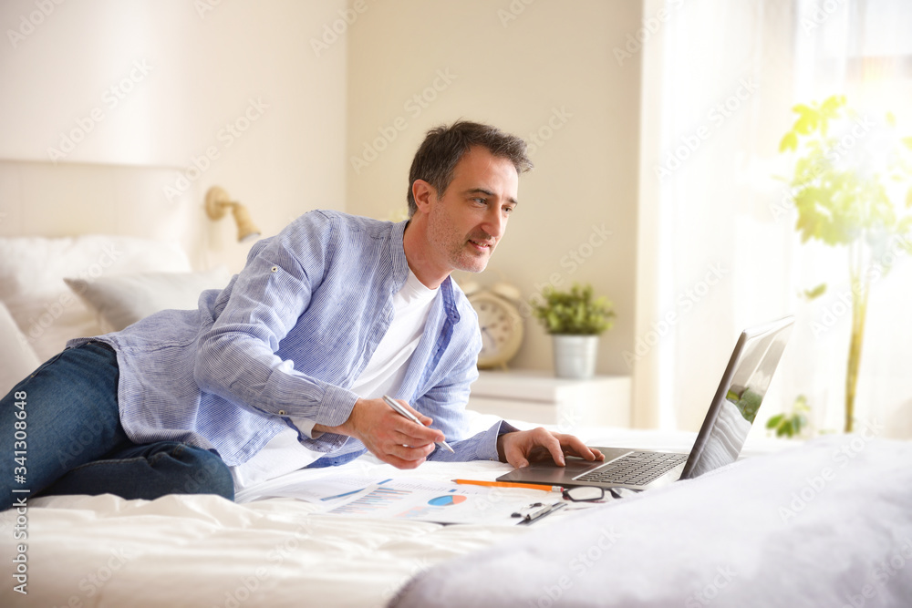 Businessman working with a laptop smiling lying on a bed