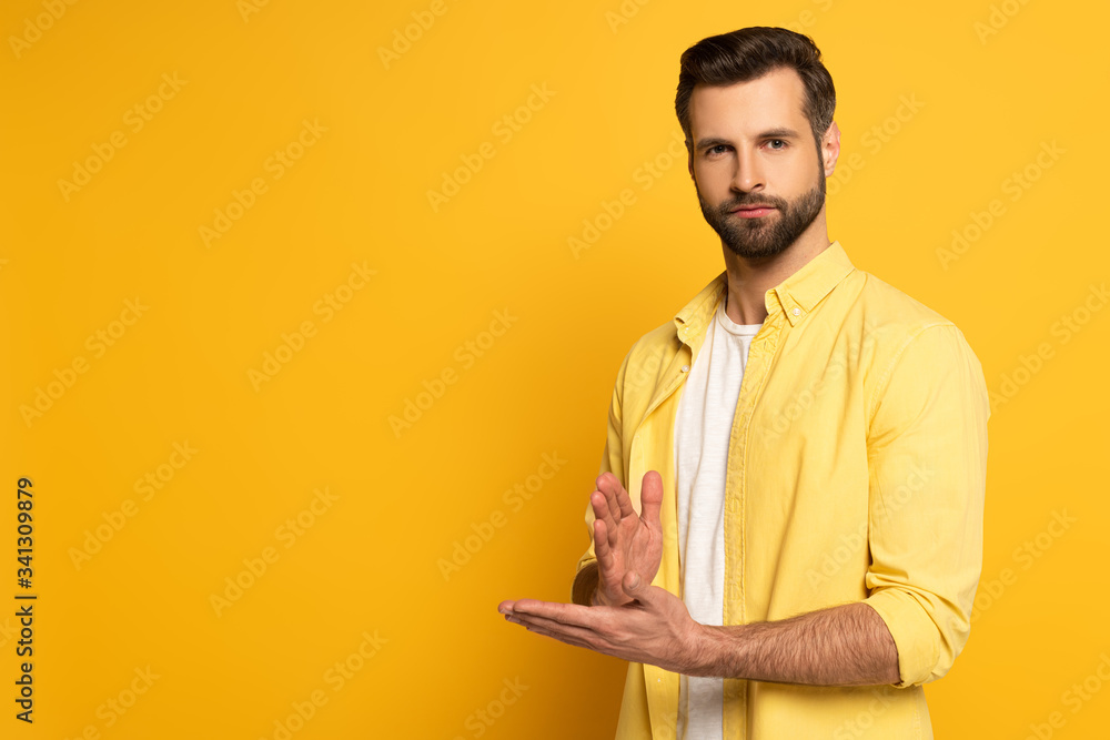 Young man looking at camera while showing gesture in deaf and dumb language on yellow background Young man looking at camera while showing gesture in deaf and dumb language on yellow background