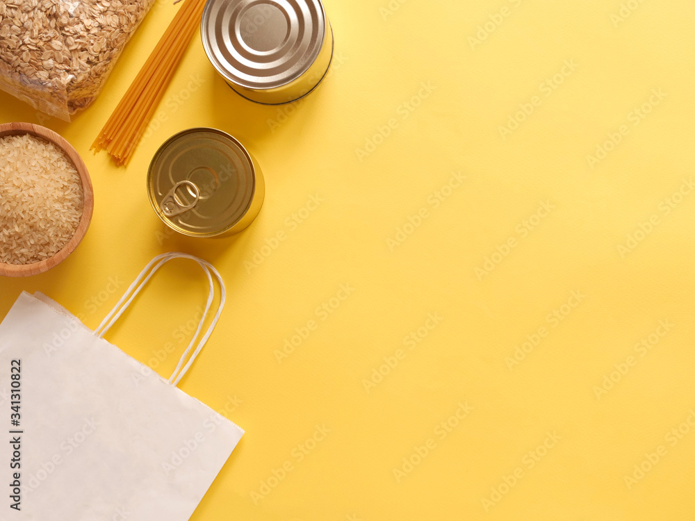 Dry goods, delivery, stockpiling, food supplies for staying home concept, donation, volunteer. Craft paper shopping bag, preserves, pasta, oatmeal, rice, on yellow background, copyspace
