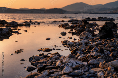 Beautiful bright sunset by the sea overlooking the hills. Rocky seashore. Natural background and texture. Shore of the Mediterranean Sea in Turkey, Bodrum.
