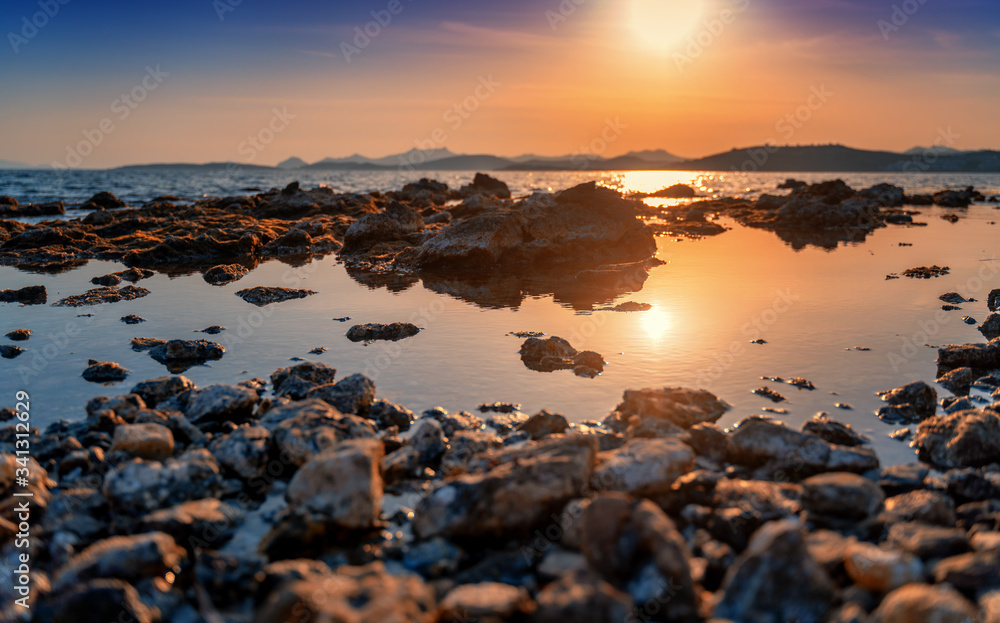 Beautiful bright sunset by the sea overlooking the hills. Rocky seashore. Natural background and texture. Shore of the Mediterranean Sea in Turkey, Bodrum.