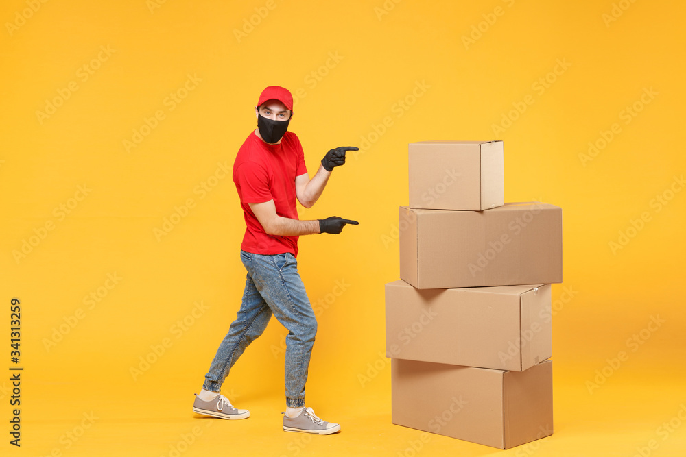 Delivery man employee in red cap blank t-shirt uniform face mask glove hold empty cardboard box isolated on yellow background studio Service quarantine pandemic coronavirus flu virus 2019-ncov concept Delivery man employee in red cap blank t-shirt uniform face mask glove hold empty cardboard box isolated on yellow background studio Service quarantine pandemic coronavirus flu virus 2019-ncov concept
