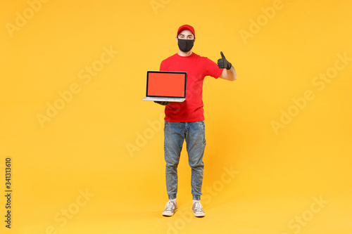 Delivery man in red cap blank t-shirt uniform mask gloves isolated on yellow background studio Guy employee work hold laptop pc computer Service quarantine pandemic coronavirus virus 2019-ncov concept