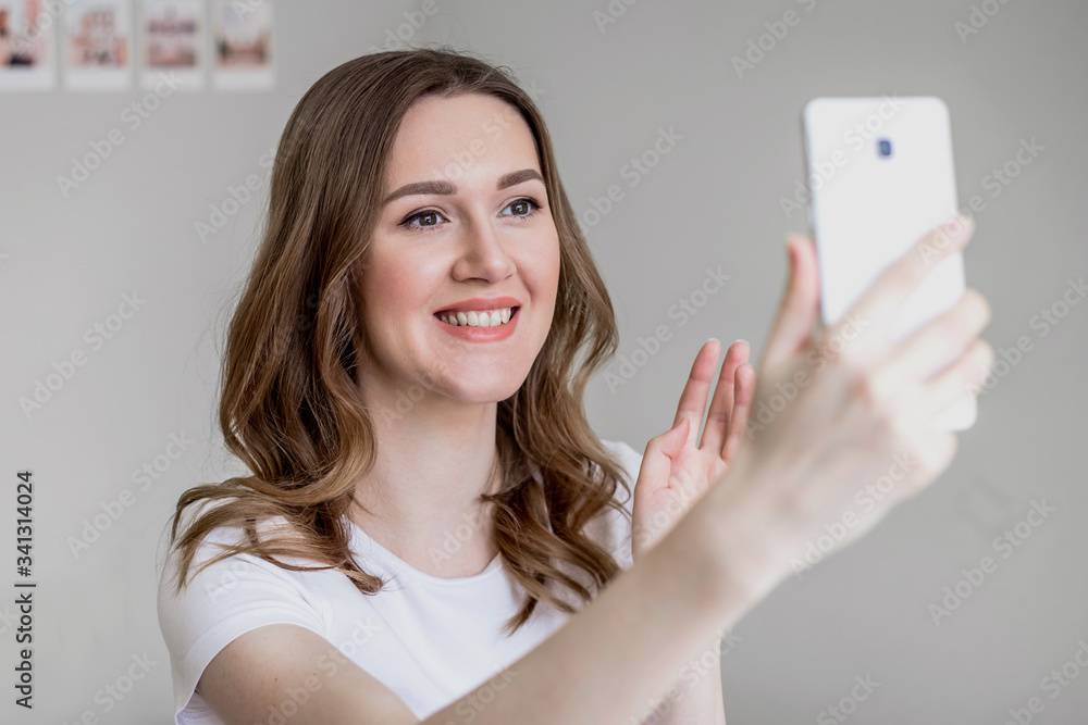 A young girl blogger smiles, holds a mobile phone in her hands and makes video calls to her friends or removes the vlog for subscribers