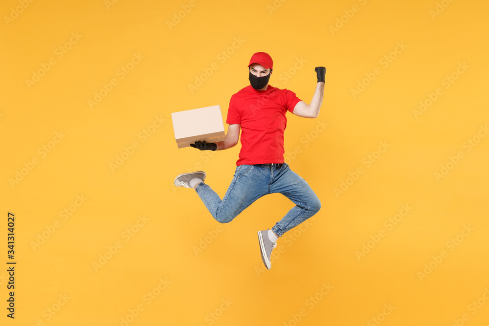 Fun jumping delivery man in red cap t-shirt uniform sterile face mask gloves isolated on yellow background studio Guy employee courier Service quarantine pandemic coronavirus virus 2019-ncov concept. - obrazy, fototapety, plakaty 