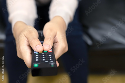 close up Television remote control in casual young female yellow shirt hands pointing to tv set and turning it on or off. select channel watching tv on sofa at home in the living room relax.