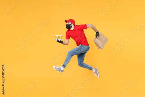 Fun jumping delivery man guy employee in red cap mask gloves hold craft paper packet food coffee isolated on yellow background studio. Service quarantine pandemic coronavirus virus 2019-ncov concept.