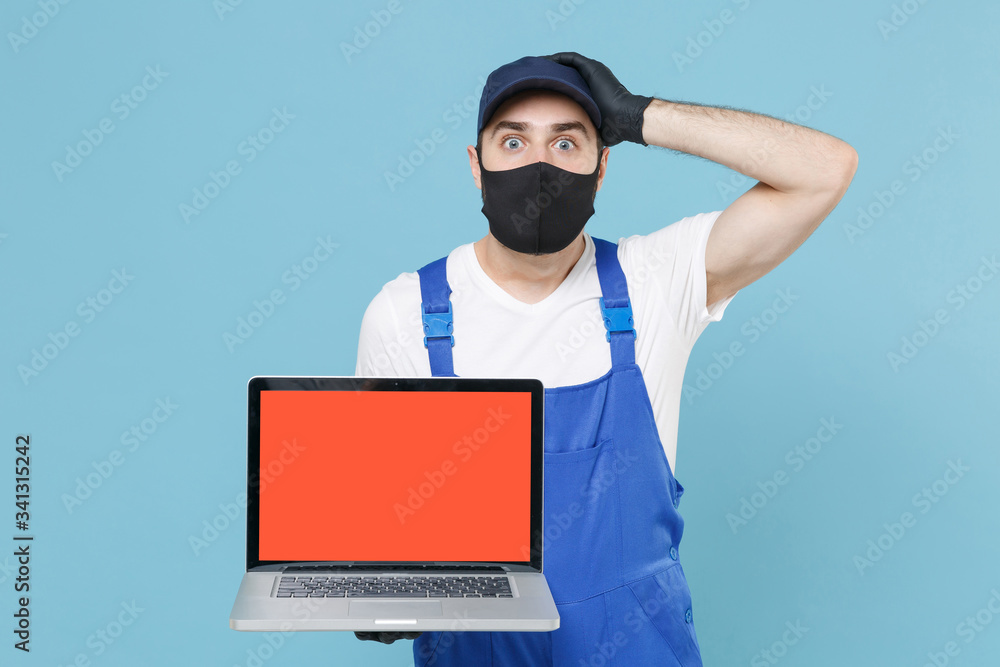 Delivery man in cap t-shirt uniform sterile mask gloves isolated on blue background studio. Guy employee courier hold laptop pc computer Service quarantine coronavirus virus covid-19 2019-ncov concept