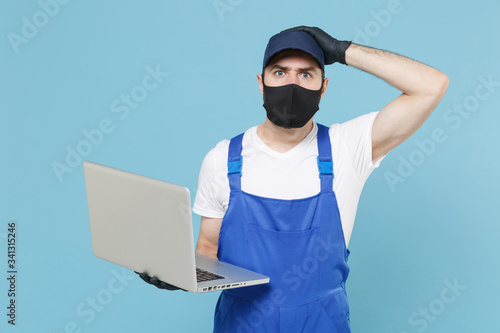 Delivery man in cap t-shirt uniform sterile mask gloves isolated on blue background studio. Guy employee courier hold laptop pc computer Service quarantine coronavirus virus covid-19 2019-ncov concept