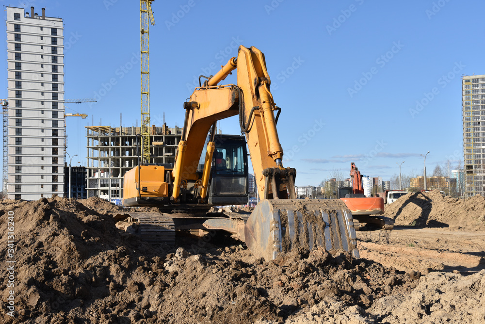 Excavators during earthmoving at construction site. Backhoe dig ground for the construction of foundation and laying sewer pipes district heating. Earth-moving heavy equipment on road works Excavators during earthmoving at construction site. Backhoe dig ground for the construction of foundation and laying sewer pipes district heating. Earth-moving heavy equipment on road works