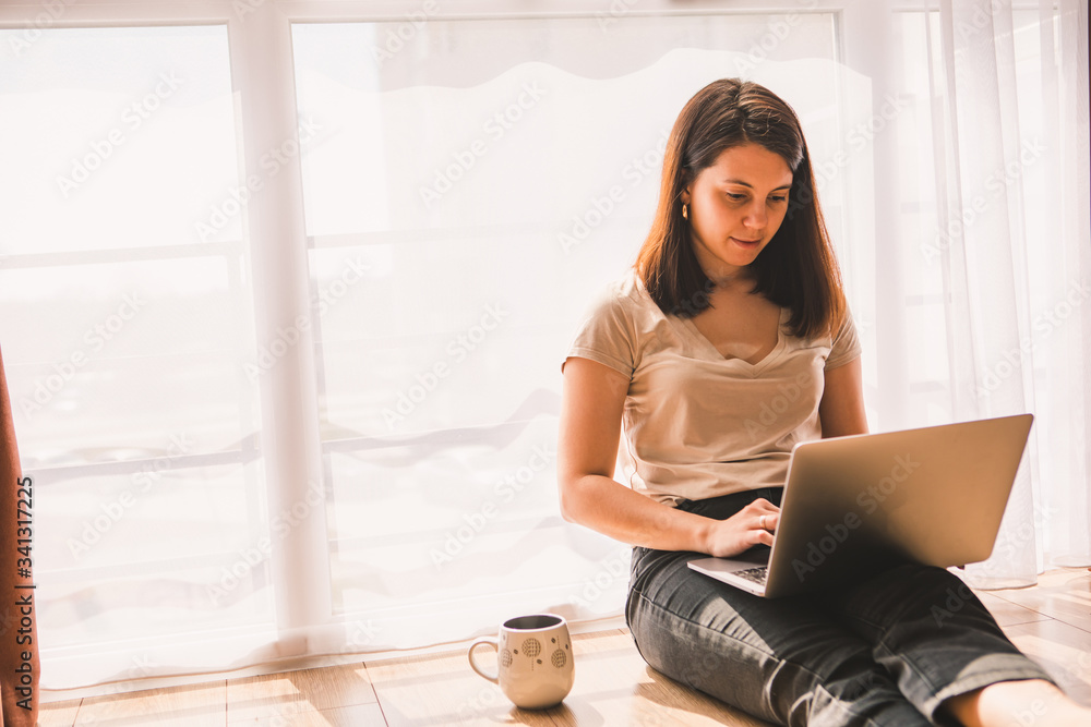 Obraz premium woman sitting on the floor working on laptop near big window