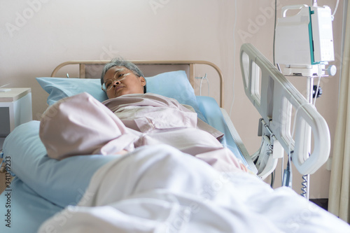 Healthcare and medical patient concept, Elder Asian people sick sitting alone on bed in hospital with medical drip intravenous needle, give salt water when her get well after treatment or surgery