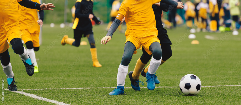 Group of Young Boys in Soccer Sportswear Running and Kicking Ball on the Soccer Grass Field. Low Angle Image of Youth Football Competition with Blurred Stadium Background Group of Young Boys in Soccer Sportswear Running and Kicking Ball on the Soccer Grass Field. Low Angle Image of Youth Football Competition with Blurred Stadium Background