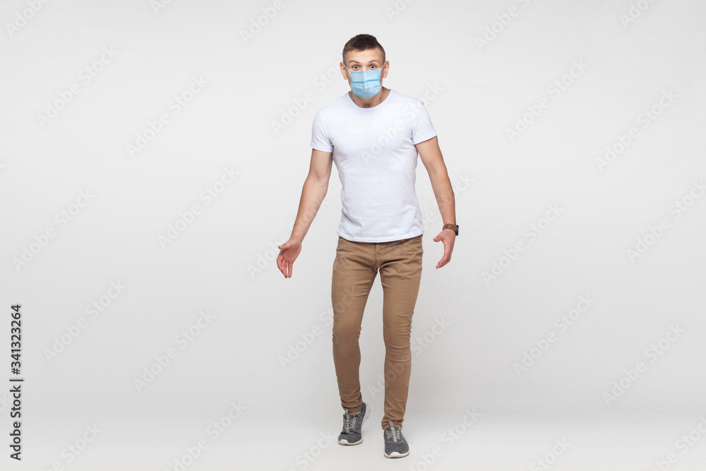 Φωτογραφία Full length portrait of amazed young man in white shirt with surgical medical mask standing with big eyes and looking at camera