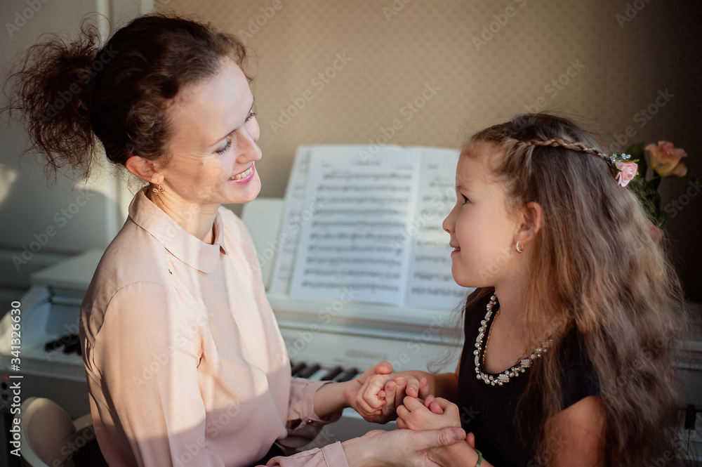 Home piano lesson. A woman and two girls practice sheet music on one musical instrument. Family concept. The idea of activities for children during quarantine.