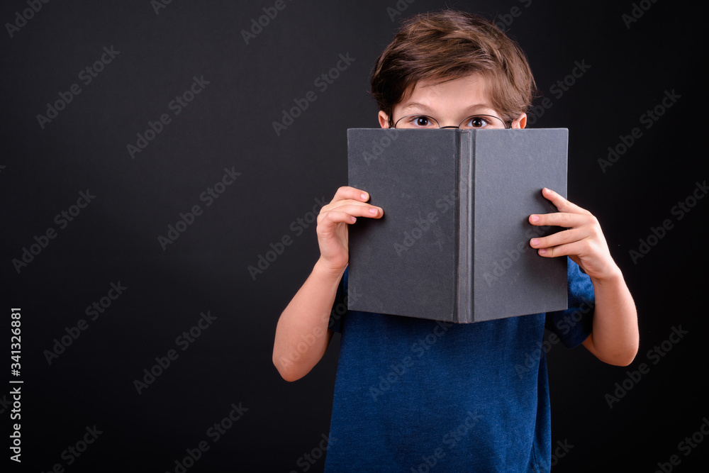 Naklejka premium Portrait of shy young boy covering face with book