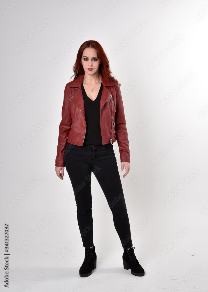 Portrait of a pretty girl with red hair wearing black jeans and boots with leather jacket. full length standing pose on a studio background. Portrait of a pretty girl with red hair wearing black jeans and boots with leather jacket. full length standing pose on a studio background.