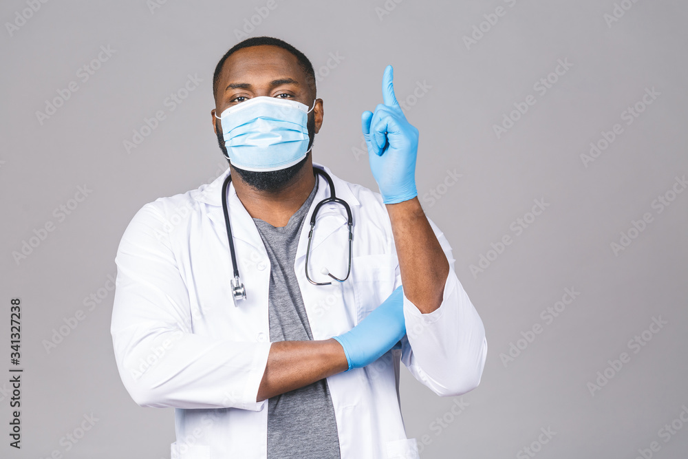 African american doctor man in medical gown sterile mask gloves isolated on grey background. Epidemic pandemic coronavirus 2019-ncov sars covid-19 flu virus. Pointing finger. African american doctor man in medical gown sterile mask gloves isolated on grey background. Epidemic pandemic coronavirus 2019-ncov sars covid-19 flu virus. Pointing finger.