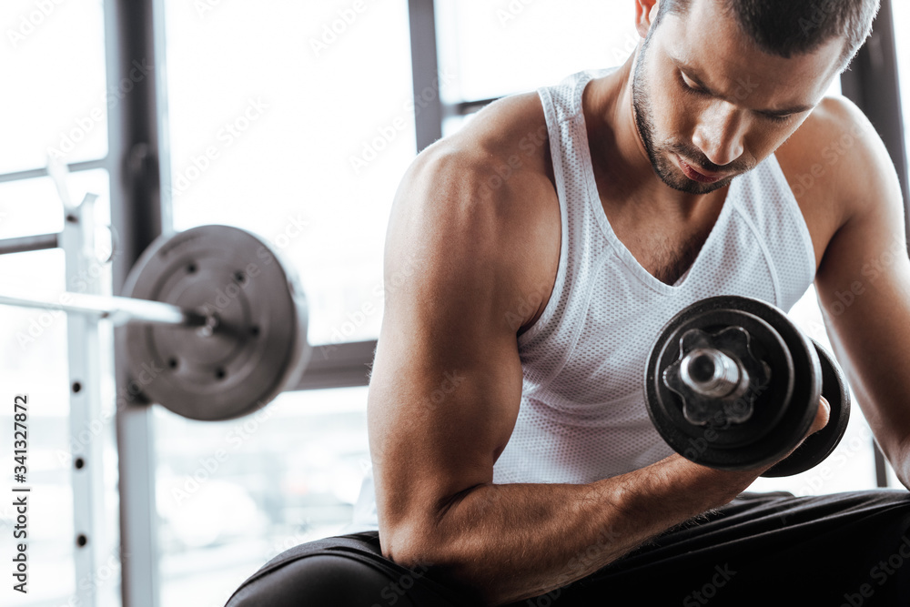 strong sportsman exercising with dumbbell while sitting in gym strong sportsman exercising with dumbbell while sitting in gym