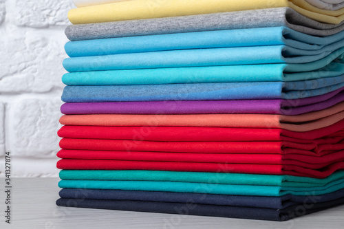 A stack of clean, neatly folded colored clothes on a light wooden table. Colors of rainbow.