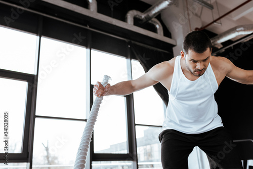 concentrated man exercising with battle rope in gym