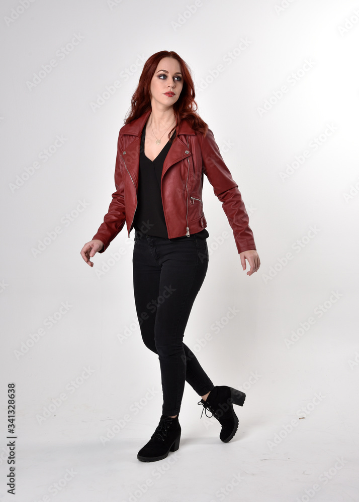 Portrait of a pretty girl with red hair wearing black jeans and boots with leather jacket. full length standing pose on a studio background. Portrait of a pretty girl with red hair wearing black jeans and boots with leather jacket. full length standing pose on a studio background.