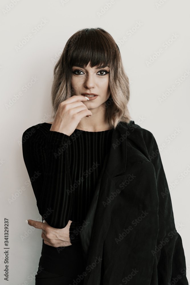 Portrait beautiful woman with attitude wearing black clothes posing on white background looking at camera touching lips Portrait beautiful woman with attitude wearing black clothes posing on white background looking at camera touching lips