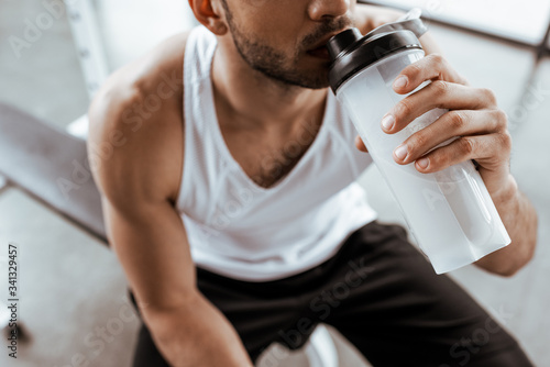 cropped view of sportsman drinking protein milkshake while holding sports bottle