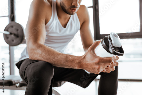 cropped view of sportsman holding sports bottle with protein milkshake in gym