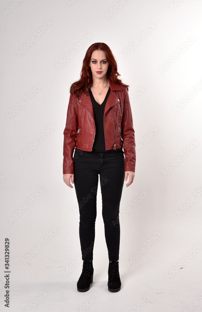 Portrait of a pretty girl with red hair wearing black jeans and boots with leather jacket. full length standing pose on a studio background. Portrait of a pretty girl with red hair wearing black jeans and boots with leather jacket. full length standing pose on a studio background.
