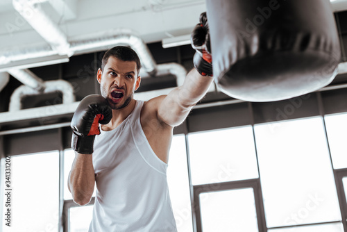 selective focus of angry man in boxing gloves exercising with punching bag