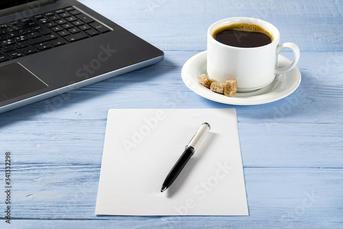 Laptop with cup of coffee on light blue old wooden table. Notebook with cup of fresh coffee in home office. Working from home concept