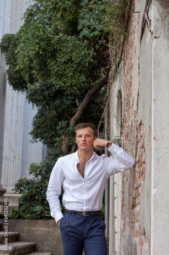 Fényképezés handsome and young guy in a white shirt enjoy the summer weather leans on a brick wall in Venice