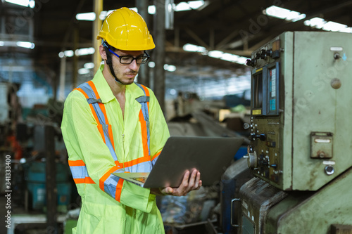 industrial man wearing uniform safety and helmet working with laptop in factory background.