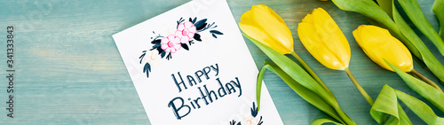 Photography panoramic shot of greeting card with happy birthday lettering near yellow tulips