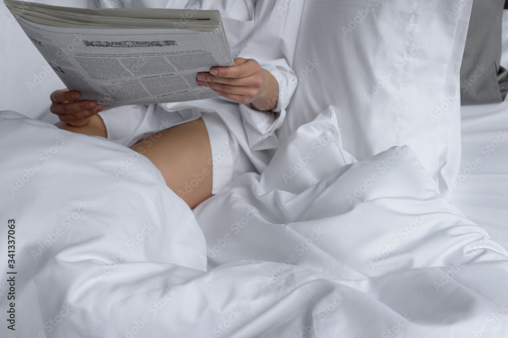 woman reads newspaper in white bedding