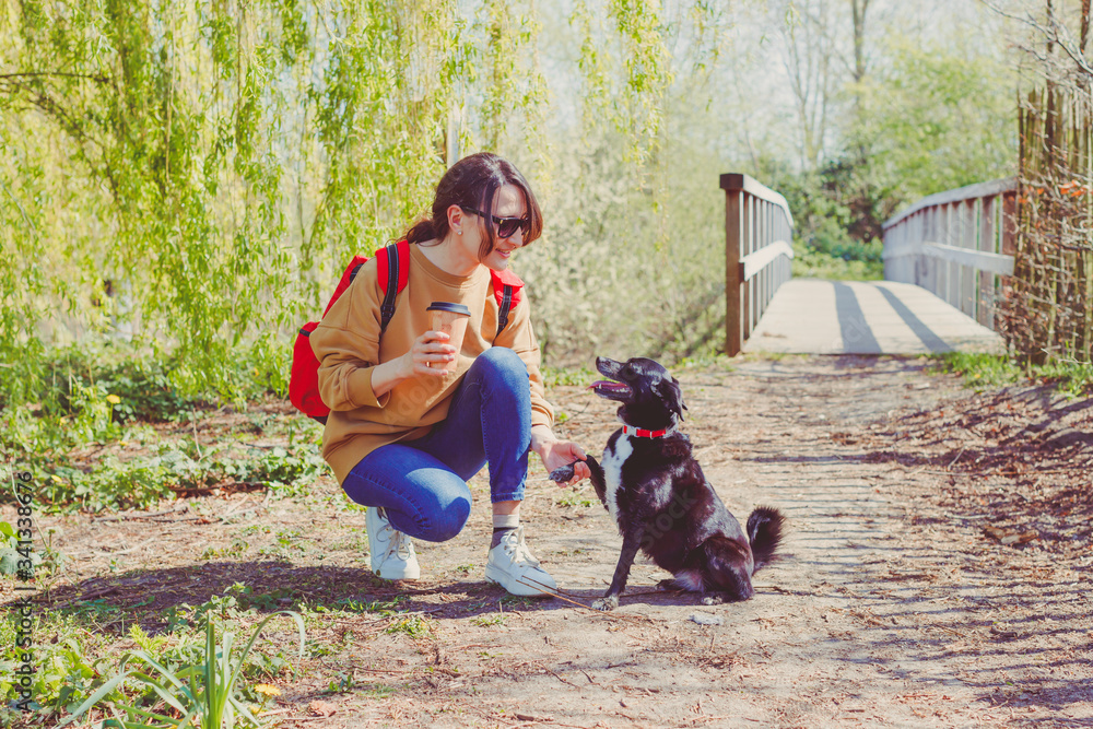 Young smiling woman with a little black dog sitting outdoors - a girl holding paw of her dog - concept of friendship, family and trust Young smiling woman with a little black dog sitting outdoors - a girl holding paw of her dog - concept of friendship, family and trust
