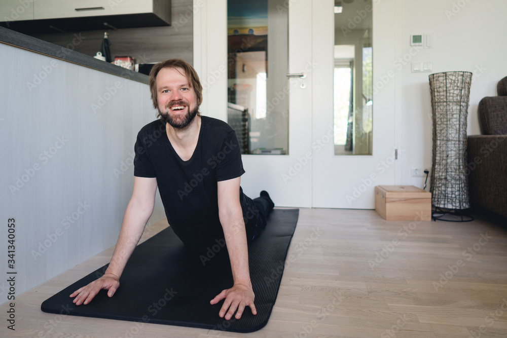 Mann macht Yoga-Übung zu Hause auf der Yogamatte und lächelt in die Kamera