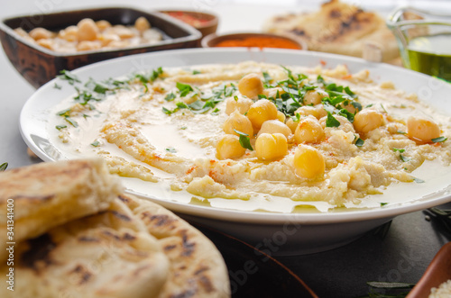 Closeup view at Hummus topped with beans olive oil and green coriander leaves on kitchen table with pita bread