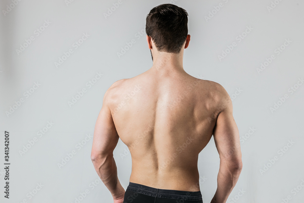 Back of a muscular bodybuilder athlete posing on a light background