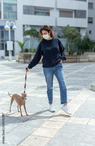 Woman in protective mask against coronavirus during quarantine walking the dog